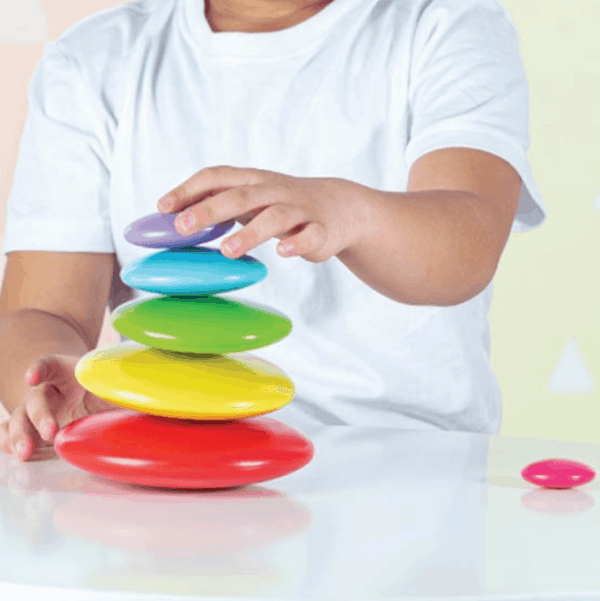 child playing with wooden rainbow pebbles stacking toy